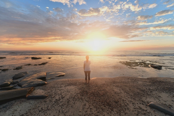 Image of a person standing on the beach at sunrise
